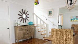 Una escalera de madera con barandas blancas, un armario de madera rústica y una silla de fibras naturales.