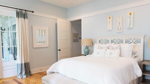 Un dormitorio con una cama grande, un banco, una puerta y una ventana con cortinas.
