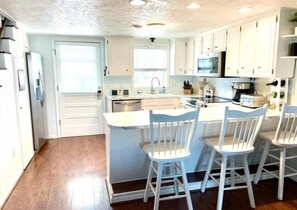 A kitchen with white cabinets, a central island with bar stools, a microwave, and a dishwasher. - Cana Front Beauty close to the Heart of OIB! (Ocean Isle Beach)