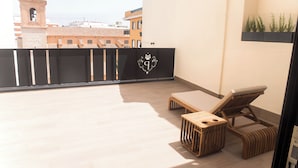 A balcony with a view of a historic building, a black gate with a crest, and a lounge chair. - Platea Concept Suites (Caudete)