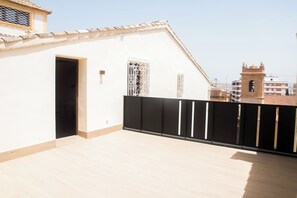 A balcony with a tiled floor, a black metal fence, and a white wall with a window. - Platea Concept Suites (Caudete)