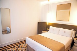 A hotel room with a bed, bedside tables, a mirror, and a patterned floor.