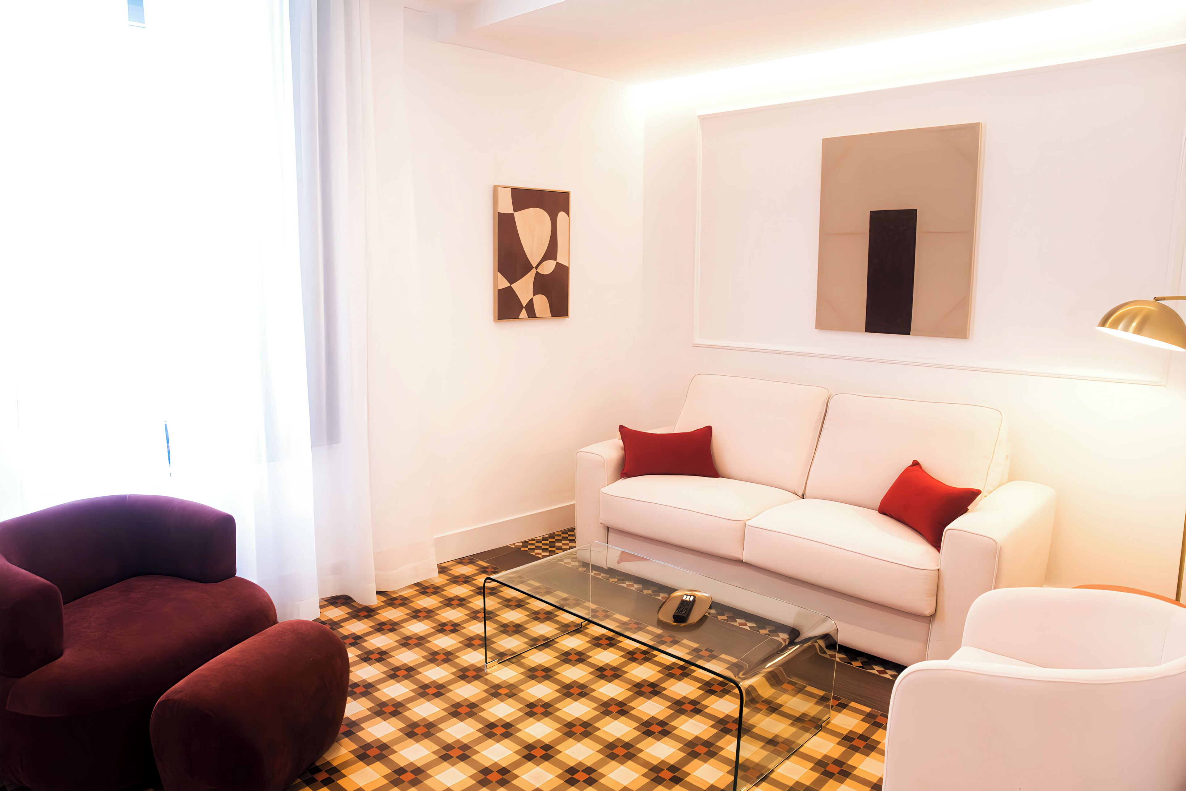 A modern living room with a white sofa, red cushions, a glass coffee table, and a patterned floor.