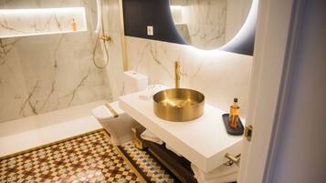 Un baño con pared de mármol, un lavamanos blanco, un grifo dorado y un suelo estampado.
