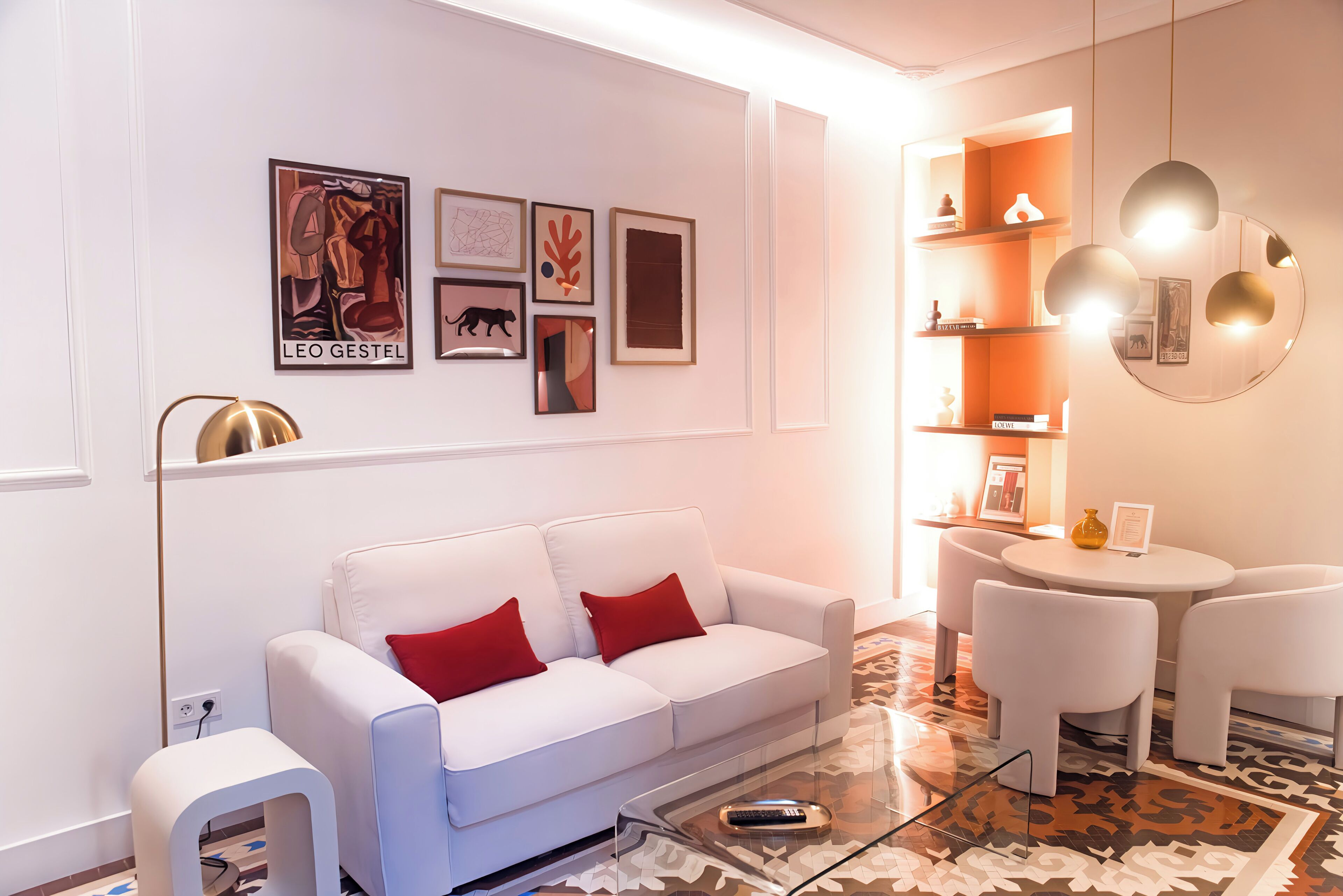 Un salon moderne avec un canapé blanc, des coussins rouges, une table basse en verre et un coin repas comprenant une petite table ronde et des chaises.