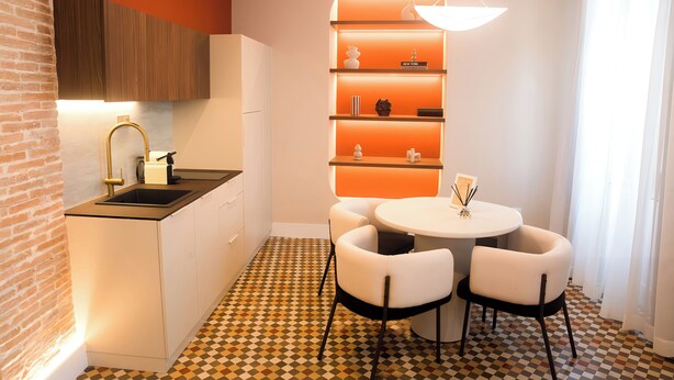 A modern kitchen with a built-in oven, a sink, and a dining area with a round table and two chairs. - Platea Concept Suites (Caudete)
