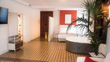 Habitación de hotel con piso estampado, una cama, una planta grande y una bañera.