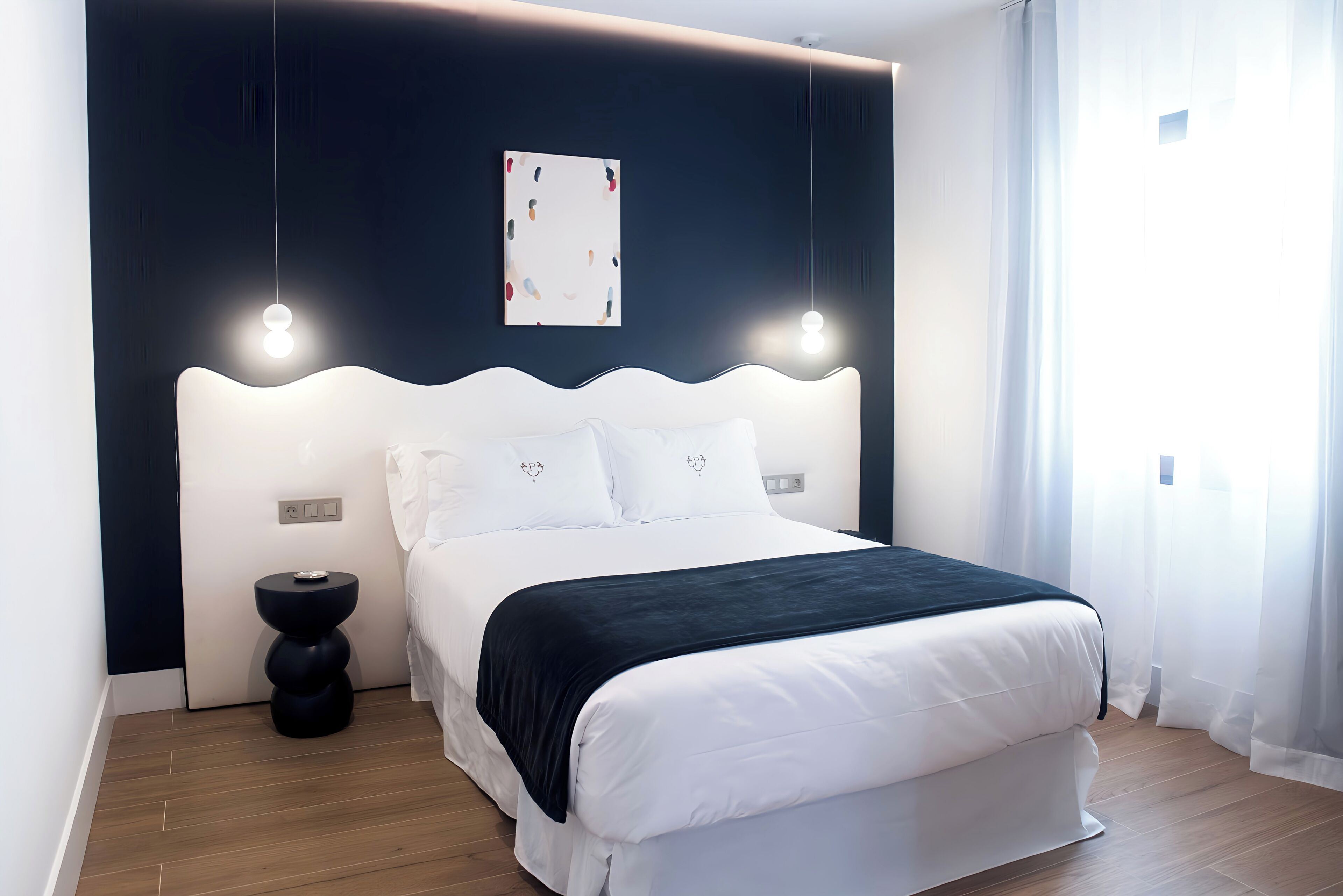 A modern bedroom with a white bed, dark headboard, and a single bedside table.
