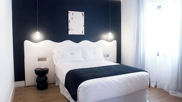 Un dormitorio moderno con una cama blanca, cabecera oscura y una mesita de noche.