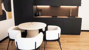 A modern kitchen with a round dining table and four chairs, a black countertop, and a single gold faucet. - Platea Concept Suites (Caudete)