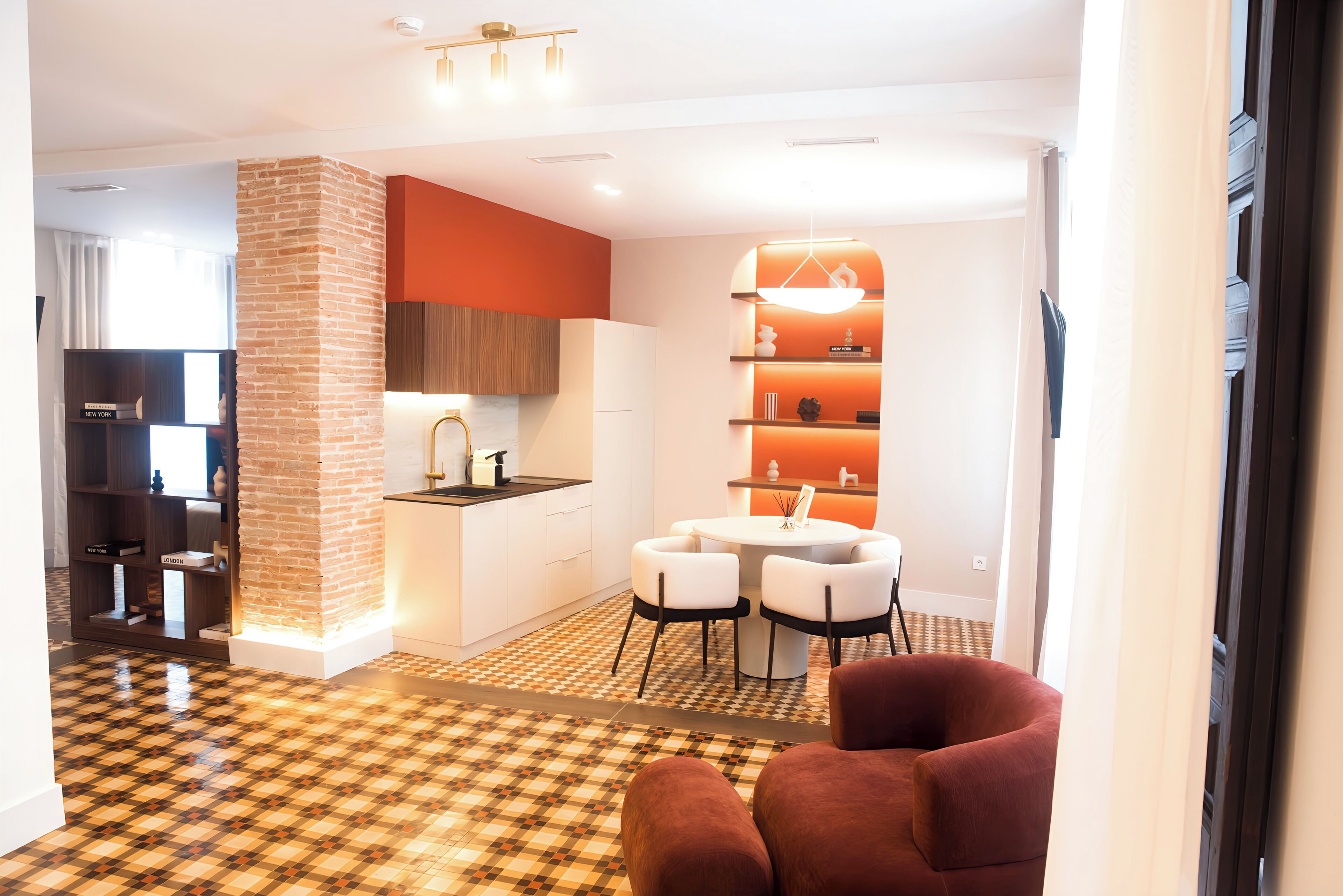 A modern kitchen with a brick accent wall, white cabinetry, and a dining area with a round table and chairs.