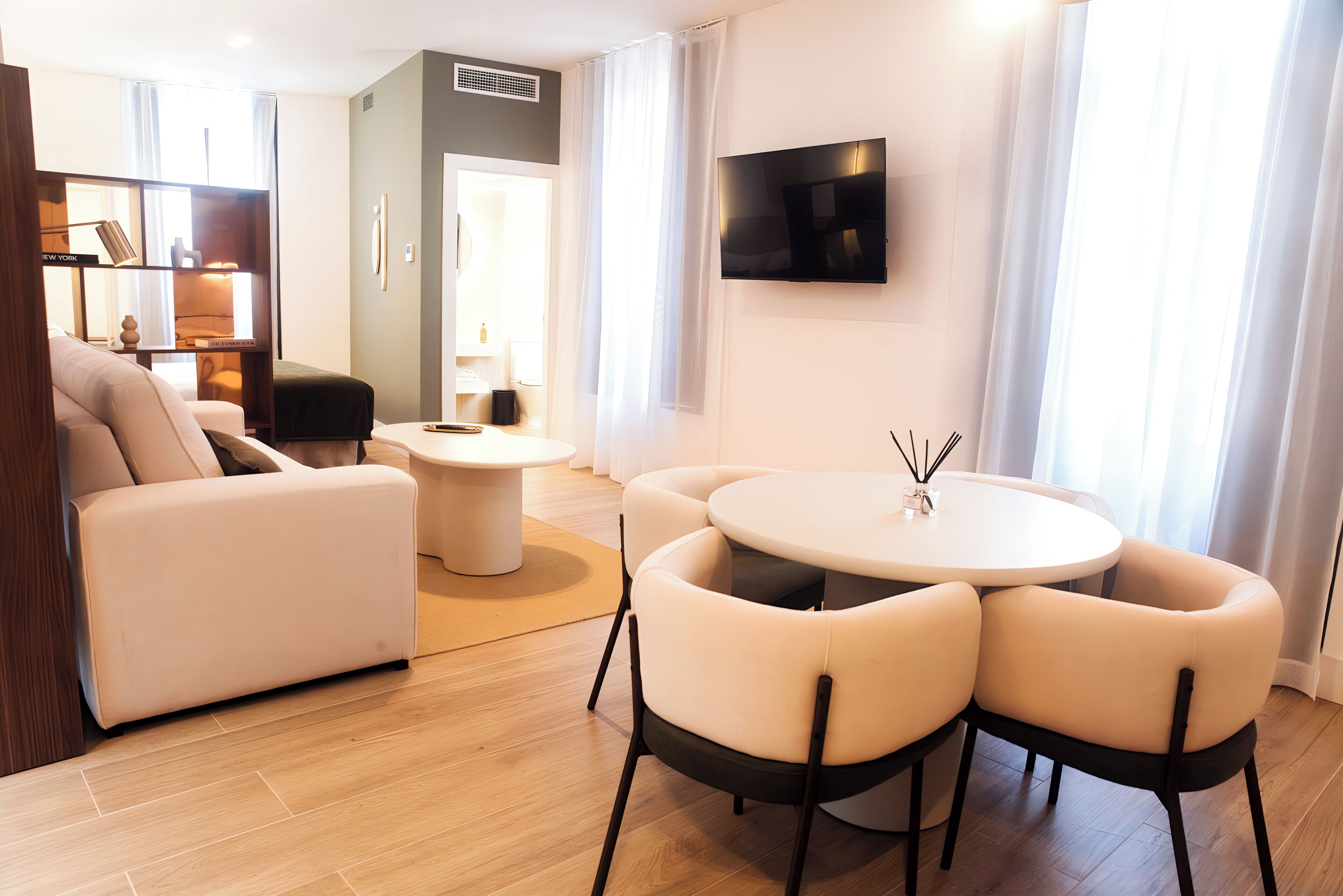 Una sala de estar moderna con un sofá, una mesa redonda con sillas, un televisor de pantalla plana montado en la pared y una estantería.