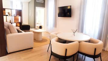 Una sala de estar moderna con un sofá, una mesa redonda con sillas, un televisor de pantalla plana montado en la pared y una estantería.