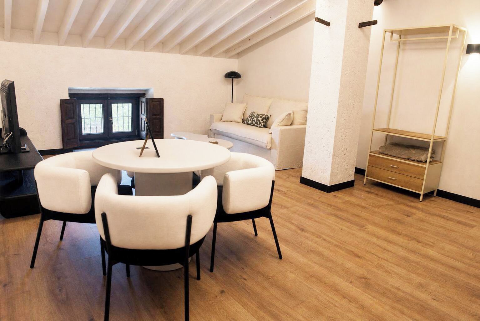 A modern living room with a round table, four chairs, a sofa, a lamp, and a wooden floor.