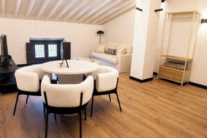 A modern living room with a round table, four chairs, a sofa, a lamp, and a wooden floor.