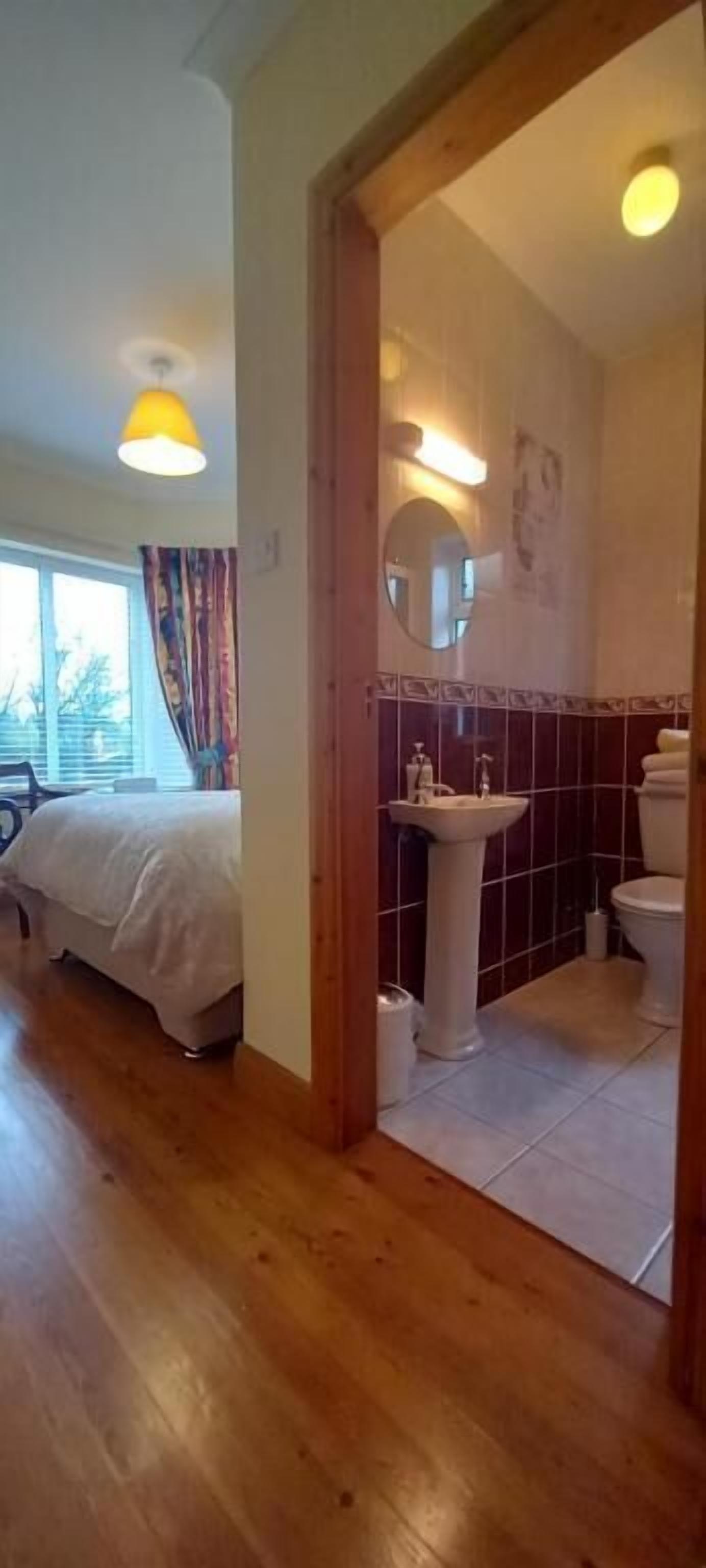 A bedroom with a bed, a bathroom with a sink and toilet, and a wooden floor.
