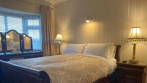 A bedroom with a wooden bed, two bedside lamps, a mirror, and a window with blinds. - Woodhaven Manor  (Galway)