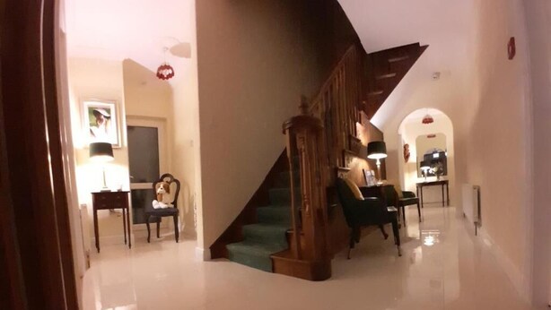 A spacious hallway with a wooden staircase, a dining area with chairs and a table, and a framed picture on the wall. - Woodhaven Manor  (Galway)