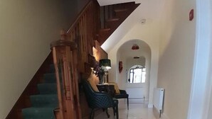 A hallway with a wooden staircase, a chair, a table, and a radiator. - Woodhaven Manor  (Galway)