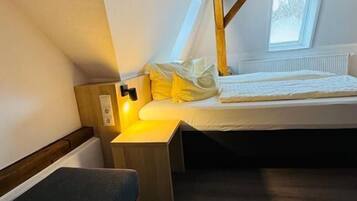 Una habitación pequeña y acogedora con cama, banca, mesita de noche y ventana.