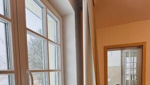 A narrow hallway with a window on the left and a door leading to a bathroom on the right.