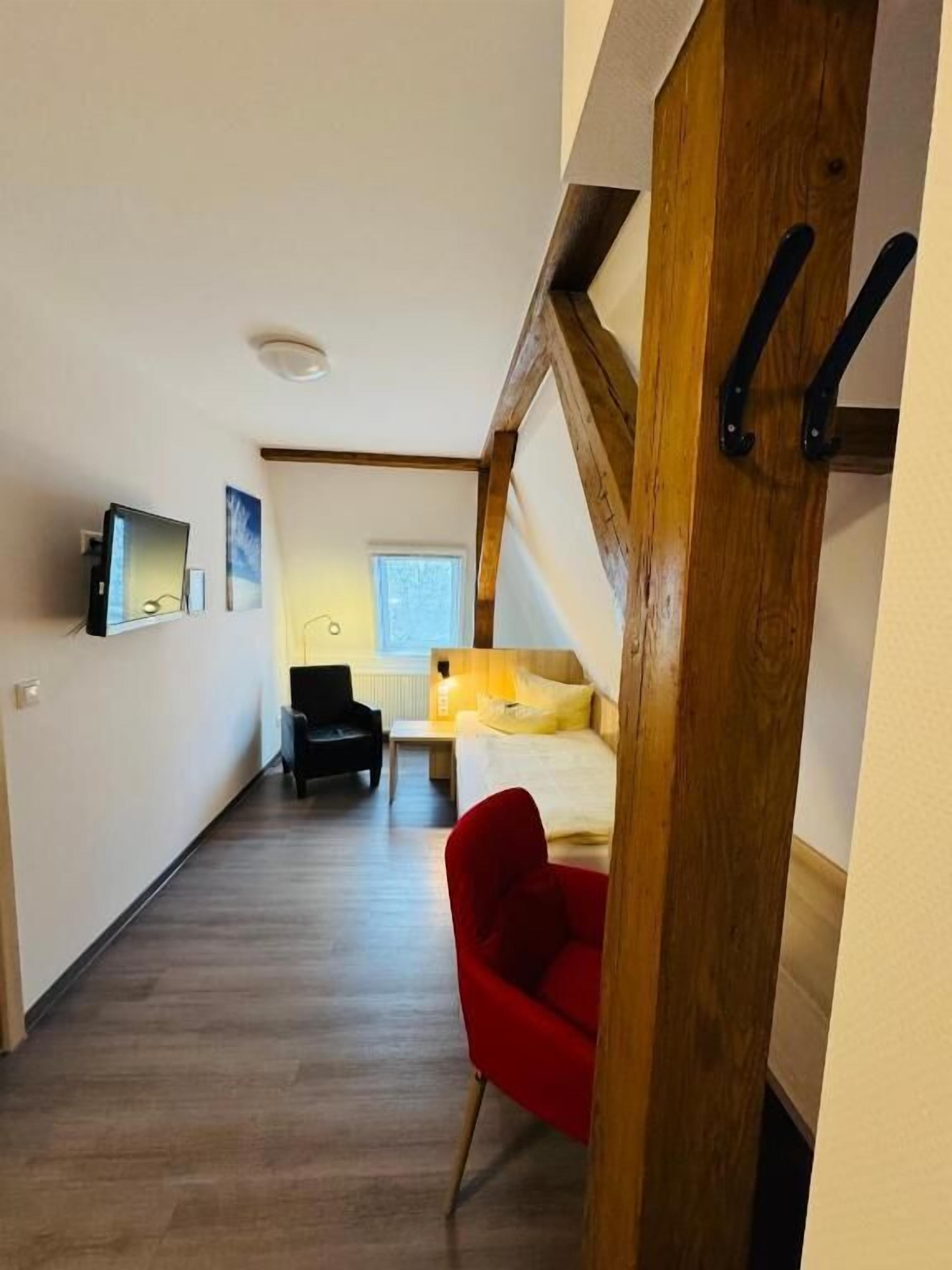 Un pasillo estrecho con una escalera de madera, una silla roja, una cama y un televisor en la pared.