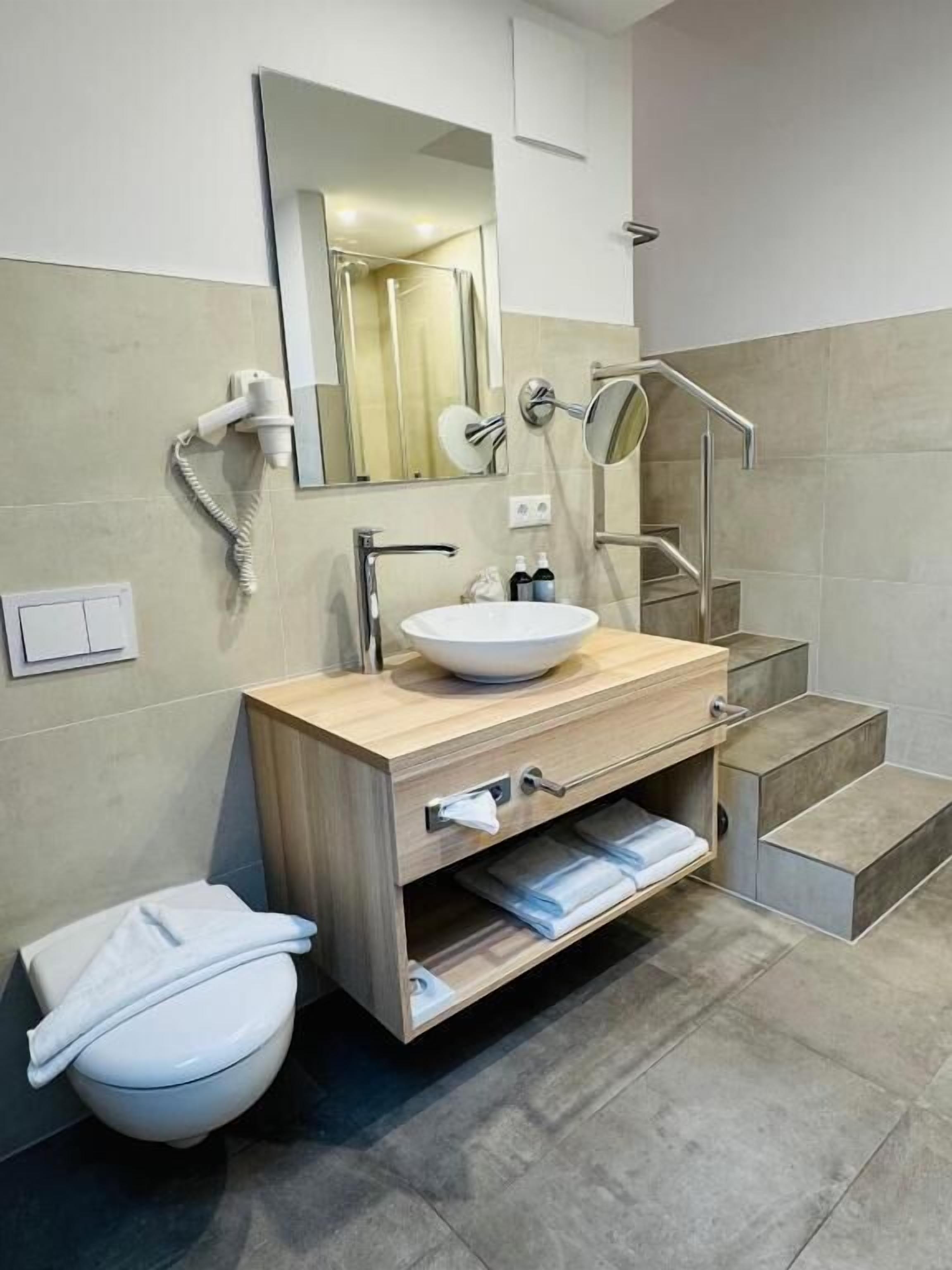 A modern bathroom with a sink, mirror, towel rack, and a toilet.
