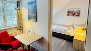 A room with a bed, a desk, and a chair. There is a window and a painting on the wall.