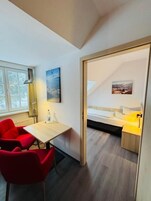 Una habitación con una cama, un escritorio y una silla. Hay una ventana y un cuadro en la pared.