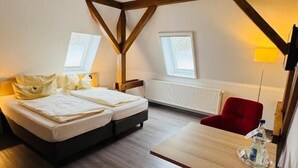 A room with a bed, a red chair, a wooden table, and a window.