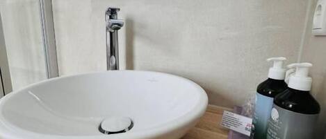 A bathroom with a white sink, a mirror, and two bottles of shampoo on a wooden countertop.