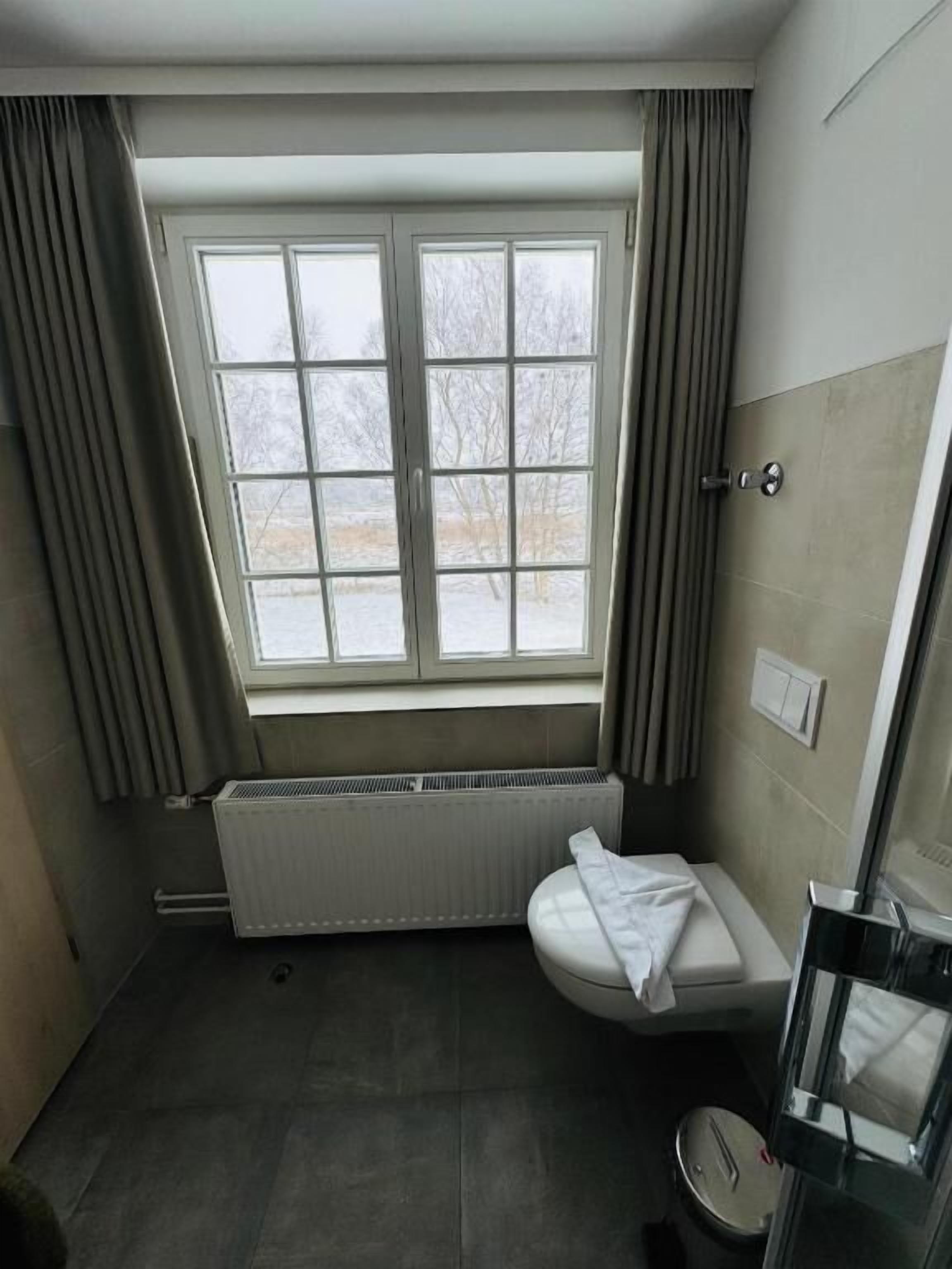 A bathroom with a window, a toilet, a radiator, and a shower area.