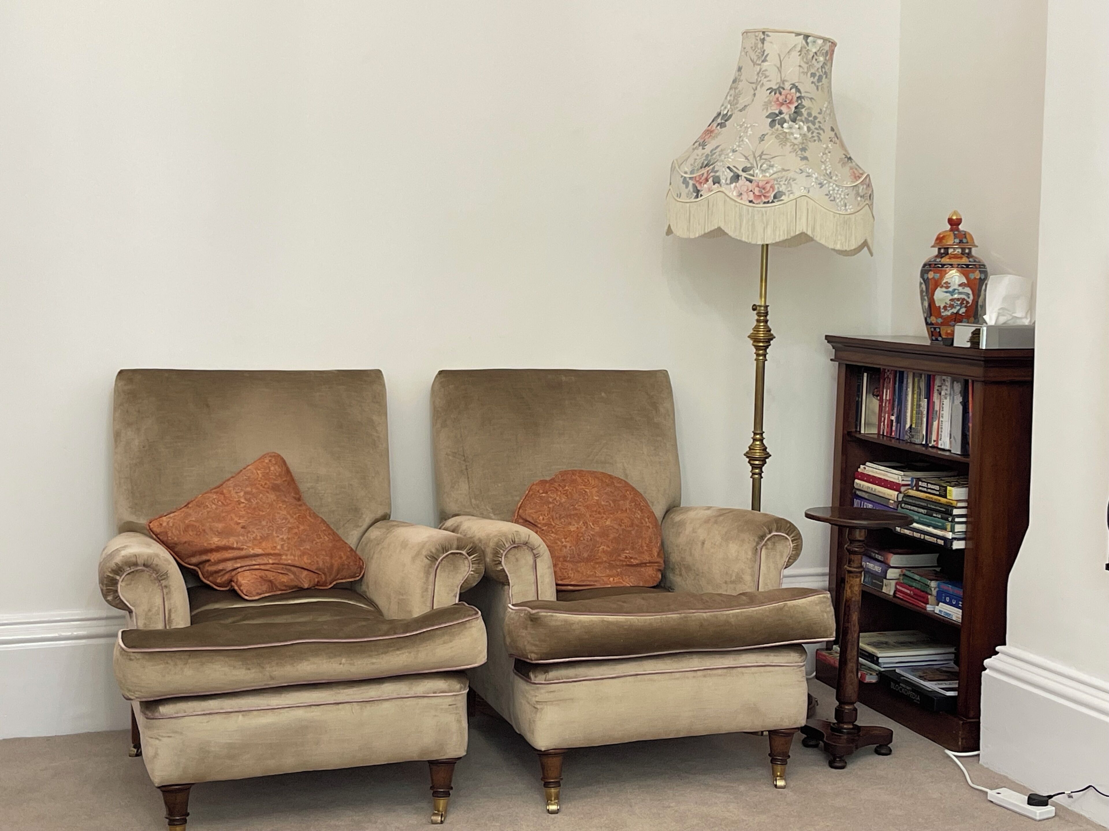 Dos sillones con cojines a juego, una lámpara de pie y una estantería llena de libros.