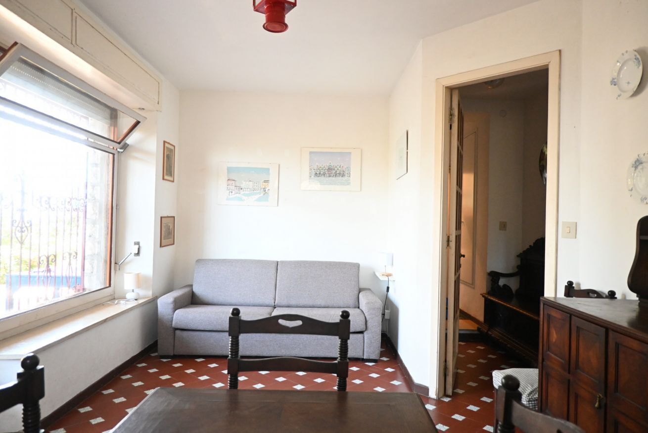 A room with a sofa, a wooden chair, a dining table, a window with blinds, and a door leading to another room.