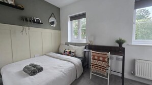 Un dormitorio con cama, mesita de noche, silla, ventana y radiador.