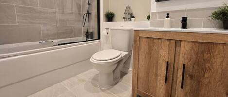 A bathroom with a bathtub, toilet, and wooden vanity.