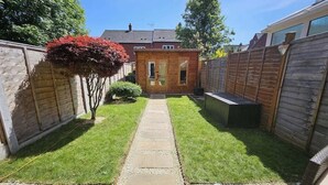 Un patio trasero con terraza de madera, un cobertizo pequeño y césped.