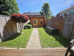 Ein Garten mit Holzterrasse, einem kleinen Schuppen und einem Rasen.
