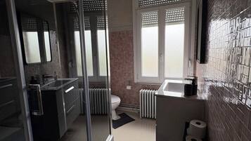 A modern bathroom with a glass shower enclosure, a toilet, a sink, and a window with blinds.