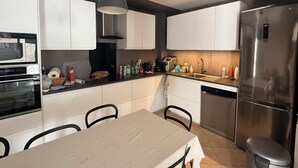 Une cuisine moderne avec des meubles blancs, un réfrigérateur en acier inoxydable, un four à micro-ondes et une table à manger avec des chaises.