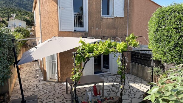 Une terrasse en pierre avec une pergola surmontée d’un parasol blanc, une chaise blanche et une petite table.