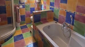 Une salle de bain avec des carreaux de couleurs vives, une douche, une baignoire avec un pommeau de douche amovible et une fenêtre avec des rideaux.