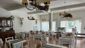 A dining area with white tables and chairs, chandeliers, and a television. - La Posada de los Robles (Las Grutas)