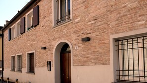 A brick building with a ground-floor entrance, windows with metal bars, and bollards along the sidewalk. - Casa Gelsomino | Private terrace, 15-minute walk to Piazza Maggiore ⭐ (Bologna)