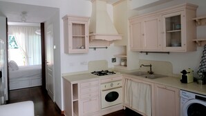A compact kitchen with a gas stove, sink, and washing machine, connected to a bedroom with a bed and a window. - Casa Gelsomino | Private terrace, 15-minute walk to Piazza Maggiore ⭐ (Bologna)