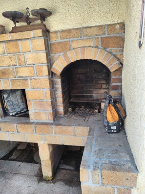 A brick-built outdoor oven with a metal grill, a bag of charcoal, and a chimney. - Villa Oasis Bollène: Master bedroom with air conditioning. Pool access. (Bollène)