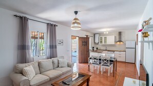 Una sala de estar con sofá, mesa de centro y comedor con sillas y una mesa. Hay una cocina con armarios y un refrigerador.