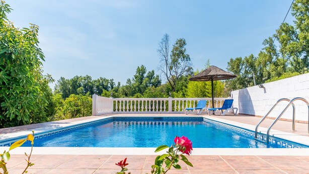 Una piscina con cerca blanca, pérgola y vistas a árboles.
