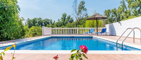 A swimming pool with a white fence, a pergola, and a view of trees.