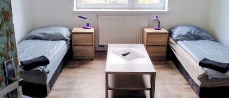 Un dormitorio con dos camas individuales, una mesa en el centro y una ventana con persianas.